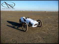 an old race car sitting in the middle of a dirt field with no one around it