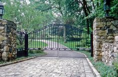 an iron gate and brick walkway leading to a driveway