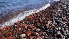 the beach is covered with rocks and pebbles as waves come in to shore on a sunny day