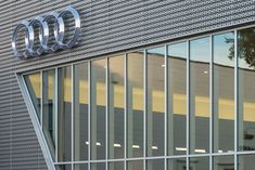 an audi logo is on the side of a building with glass windows and a tree in front of it