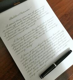 a pen sitting on top of a piece of paper next to an open notebook with cursive writing