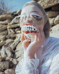 a woman in white dress holding her face up to her mouth with teeth and beads on it