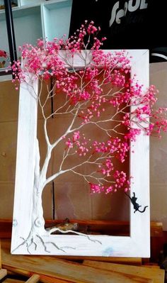 a white frame with pink flowers and a tree in the middle is sitting on a table