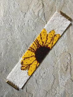 a yellow and white beaded wristband with a flower on it's side