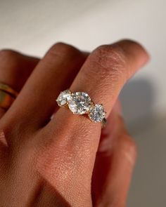 a woman's hand holding an engagement ring with three diamonds on top of it