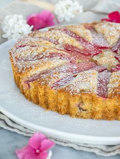 a cake with powdered sugar on top sitting on a white plate next to pink flowers