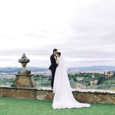 a bride and groom pose for a wedding photo in front of an italian countryside view