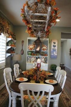 a dining room table with white chairs and fall decorations