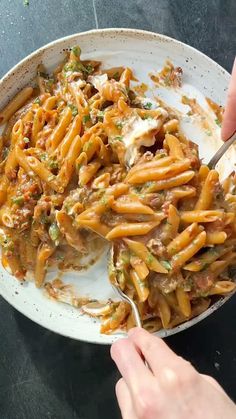 someone is eating pasta with meat and sauce in a white bowl on a black table