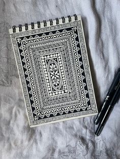 a black and white notebook sitting on top of a bed next to a pen