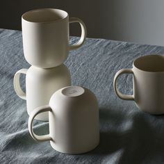 three white coffee mugs sitting on top of a blue tablecloth covered table cloth