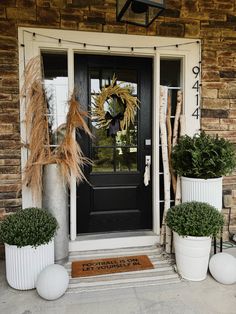 two large white planters are sitting in front of a black door with the words welcome on it