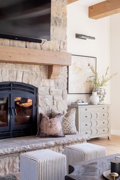 a living room with a stone fireplace and tv above the fireplace is a striped ottoman