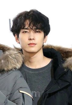 a young man wearing a black jacket and grey shirt with a fur lined hoodie