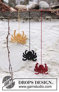 two crocheted crabs hanging from strings on a white wall with branches and rocks in the background