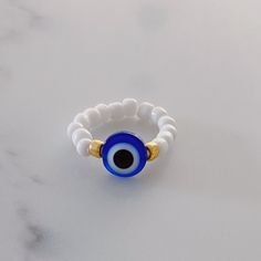 a blue and white beaded ring with an evil eye on the middle, sitting on a marble surface