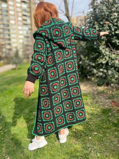 a woman standing in the grass with her arms spread out, wearing a green and red patterned coat