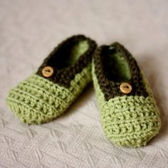 two crocheted green slippers are laying on a white sheet and one has a button in the middle