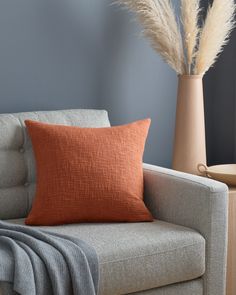 an orange pillow sitting on top of a couch next to a vase with dry grass in it