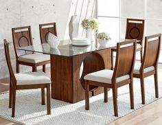 a glass dining table with wooden chairs and white vases on the top, in front of a window