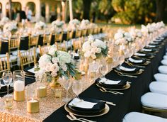 a long table is set up with black and white linens, silverware, and gold chargers