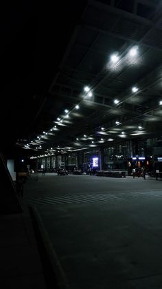 an empty parking lot at night with lights on the ceiling and cars parked in front of it