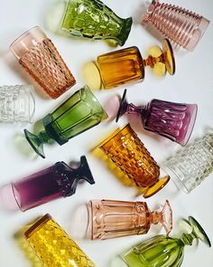 many different colored glass vases lined up on a white surface with one empty bottle in the middle