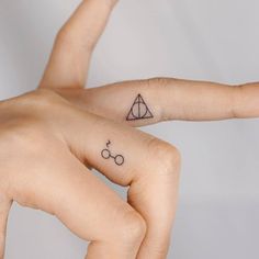 two fingers with harry potter symbols tattooed on each finger, one pointing at the other