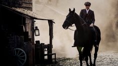 a man riding on the back of a black horse next to a barn and building