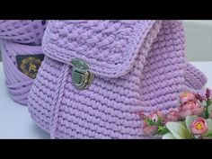 a purple crocheted purse sitting on top of a white table next to flowers