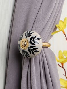 a close up of a curtain with a ring on it's end and yellow flowers in the background