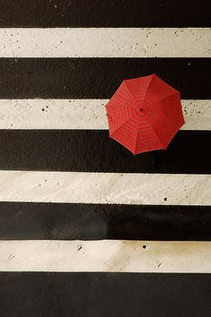 an overhead view of a red umbrella on a black and white crosswalk with stripes