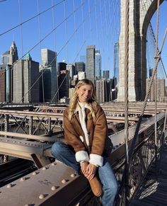 a woman sitting on the edge of a bridge in front of a cityscape