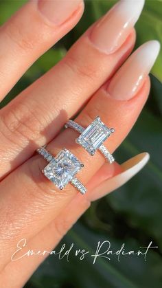 a woman's hand holding two engagement rings with diamonds on top and bottom, in front of her