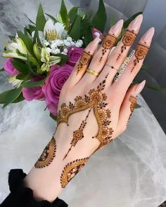 a woman's hand with henna tattoos on it and flowers in the background