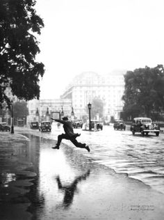 a person jumping in the air while holding an umbrella on a rainy day with cars and buildings in the background