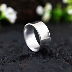 a silver ring sitting on top of a black surface next to white and green flowers