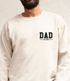 a man wearing a white sweatshirt with the word dad printed on it, standing in front of a wall