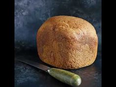 a loaf of bread next to a knife on a black surface with a gray background