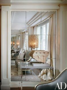 a mirrored wall in a living room next to a chair and table with a chandelier hanging from the ceiling