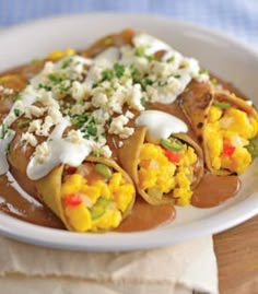 a white plate topped with tacos covered in sauce and toppings on top of a wooden table