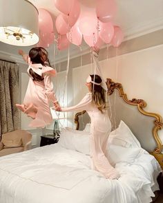 two girls jumping on a bed with pink balloons