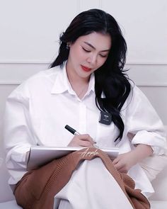 a woman sitting down writing on a piece of paper with a pen in her hand