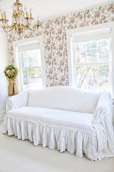 a white couch sitting under a window next to a chandelier in a living room