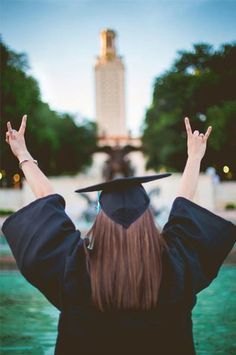 a woman wearing a graduation cap and gown raises her hands in the air