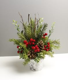 a white vase filled with red berries and greenery sitting on top of a table