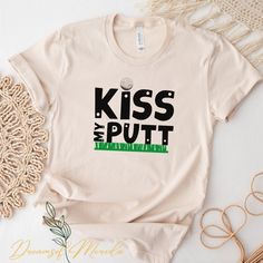 a t - shirt that says kiss the putt and is on top of a table