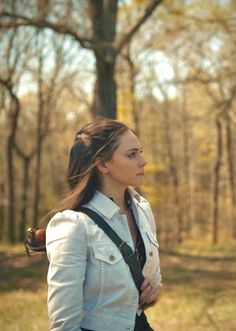 a woman standing in the woods with her back to the camera and looking off into the distance