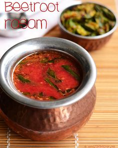 two bowls of food sitting on top of a wooden table next to silver spoons