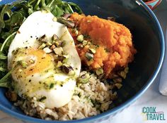 a blue bowl filled with rice and vegetables next to an egg on top of it